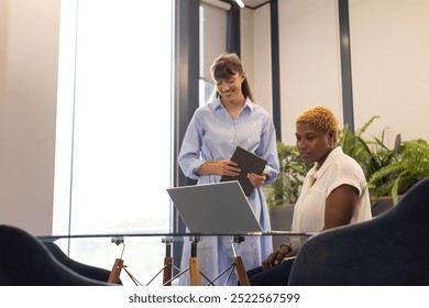 Collaborating in office, two women using laptop and digital tablet at desk. Business, teamwork, collaboration, technology, coworkers, brainstorming