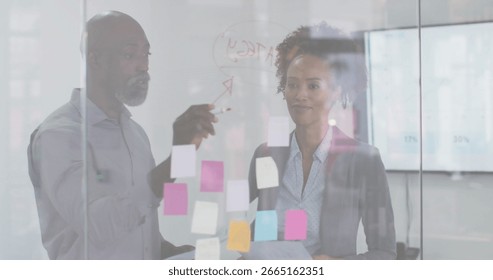 Collaborating professionals annotating glass wall in office area, with red marker and sticky notes. Collaboration, brainstorming, innovation, teamwork, modernity, creative, productivity