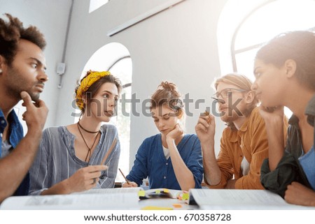 Collaboration and brainstroming concept. Portrait of interracial friends gathering together sitting at table in classroom surrounded with books having debates expressing their opinions and views.