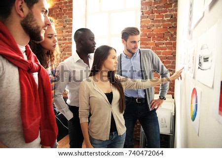 Collaboration is a key to best results. Group of young modern people in smart casual wear planning business strategy while young woman pointing at infographic displayed on the white wall in the office