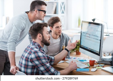 Collaboration is a key to success. Three young business people discussing something while looking at the computer monitor together 