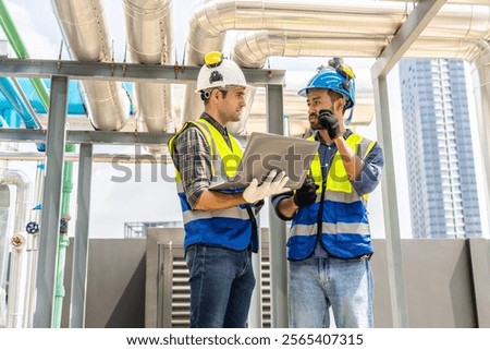 Collaboration, Two young construction workers discuss plans while reviewing blueprints on a rooftop. They wear safety gear and oversee intricate piping systems amidst a bustling urban backdrop,