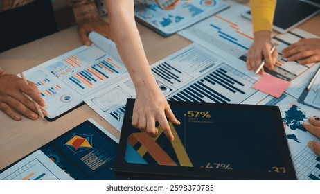 A collaborative business meeting scene where diverse professionals analyze charts and graphs on a table filled with documents and a laptop, showcasing teamwork and strategy. SACTR