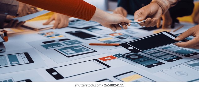 A collaborative design session showcasing hands actively engaged in smartphone and tablet prototypes on a workspace. Ideal for illustrating teamwork and innovation in user experience design. SACTR