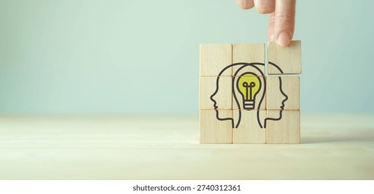Collaborative Idea Generation. A hand stacks wooden blocks forming two people with a glowing lightbulb, symbolizing teamwork, brainstorming, innovation and shared problem solving.