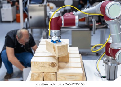 Collaborative industrial robot arm operating alongside blurred human worker while stacking wooden blocks in a smart factory environment