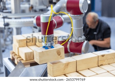 Collaborative industrial robot arm operating alongside blurred human worker while stacking wooden blocks in a smart factory environment
