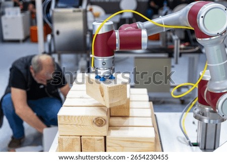 Collaborative industrial robot arm operating alongside blurred human worker while stacking wooden blocks in a smart factory environment