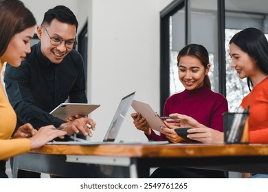 Collaborative meeting with four professionals using tablets and laptops, sharing ideas and discussing projects in modern office. Their expressions show engagement and teamwork.