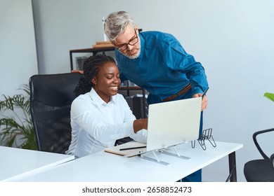 Collaborative office interaction between a senior male mentor and a young female professional, brainstorming together using a computer..
