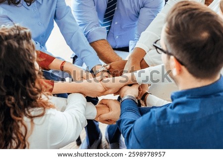 Collaborative team members join hands in a show of solidarity, bond, and shared purpose, depicting a harmonious working relationship and shared commitment. Vibrant office setting symbolizes teamwork