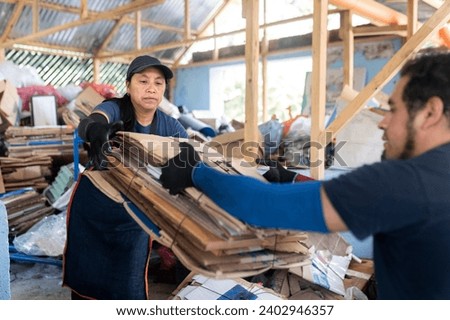 Collaborative teamwork in recycling as a young Hispanic woman receives a stack of recycled cardboard from her partner at a recycling facility.