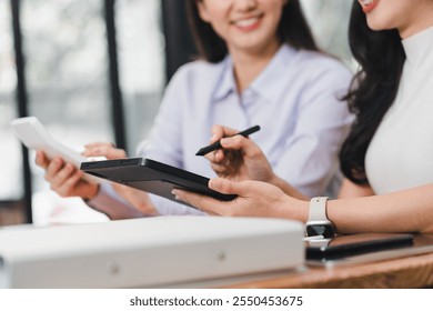 Collaborative work between two women using tablet and notebook, showcasing teamwork and creativity in modern office setting.