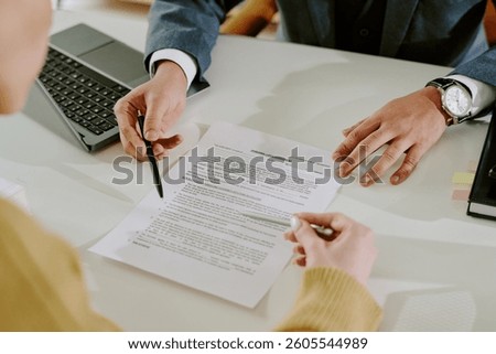 Collaborative work setting in office with people signing business document with laptop and other office supplies. Visible documents capture business focus without cluttering space