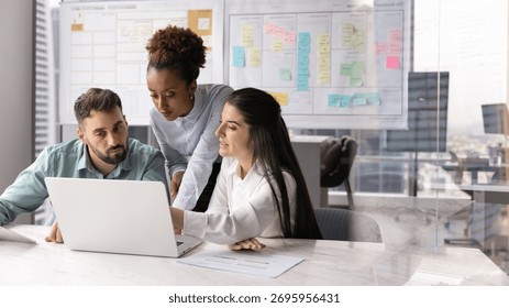 Collaborative workflow planning. Busy concentrated international business team of two diverse workers and female leader engaged in developing marketing project on notebook in Agile office. Copy space - Powered by Shutterstock - Get 15% off with code: PIKWIZARD15