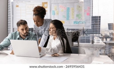 Collaborative workflow planning. Busy concentrated international business team of two diverse workers and female leader engaged in developing marketing project on notebook in Agile office. Copy space