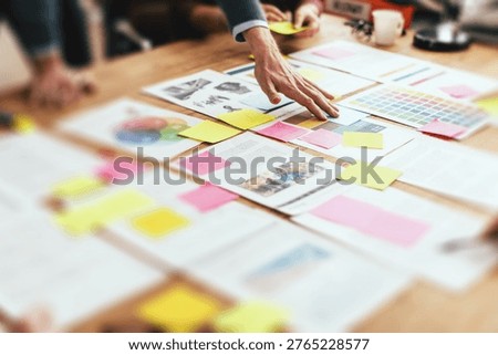 A collaborative workspace with hands reaching over documents, charts, and colorful sticky notes, suggesting a team brainstorming session.