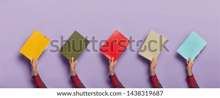 Collage image of various colorful textbooks in male hands isolated over purple background. Books for studying. Education concept. Notepads for writing notes with colored bookmarks. Horizontal shot