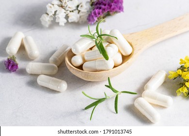 Collagen capsules for skin and beauty in the wooden spoon with herbs and flowers on white marble table close up. Health care concept.