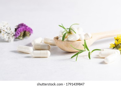 Collagen capsules for skin and beauty in the wooden spoon with herbs and flowers on white marble table close up. Health care concept.