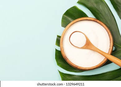 Collagen powder in bowl and measure spoon on palm leaf background. Extra protein intake. Natural beauty and health supplement. Plant based collagen concept. Flatlay, top view. Copy space.