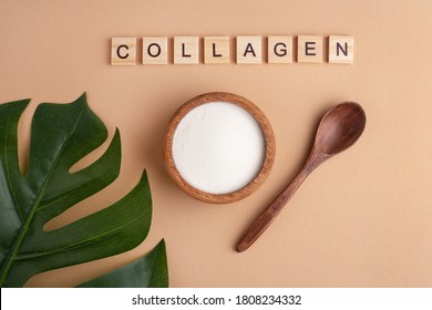 collagen powder in a wooden bowl, spoon, peach background, top view, green leaf, lettering
