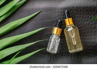 Collagen Serum Or Hyaluronic Serum In Dropper On Black Color Crocodile Skin Texture Background With Palm Leaves. Skincare Cosmetic Product Bottle. Cosmetics Health Face Skin Beauty