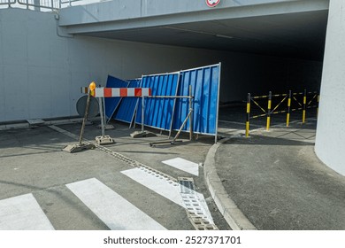 Collapsed construction barricade causing road closure under a bridge, related to traffic disruptions and urban maintenance issues