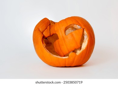 A collapsed and decayed Jack-o'-lantern with a broken face sits on a white background, showing signs of aging