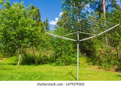 Collapsible Outdoor Clothes Dryer View. Rotary Washing Line Air Clothes Dryer Aluminum. Green Trees And Blue Sky With White Clouds Background. Sweden.