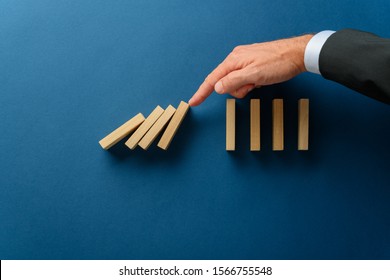 Collapsing dominos being stopped my a crisis business manager in a conceptual image. Over navy blue background with copy space. - Shutterstock ID 1566755548