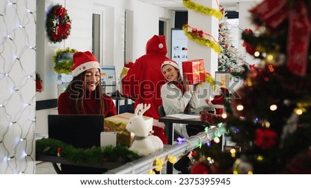 Colleague dressed as Santa spreading holiday joy in xmas ornate office, offering presents to staff members. Man in festive workspace wearing costume surprising multiethnic team with Christmas gifts