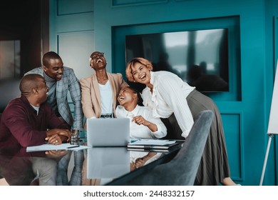 Colleagues in a boardroom have a successful business meeting. Business men and women collaborate using laptops, tablets, and computers. The group is happy, laughing, and smiling, showcasing teamwork. - Powered by Shutterstock