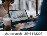 Colleagues in an coffee bar meeting reviewing a sales chart on a laptop screen with coffee cups on the desk.