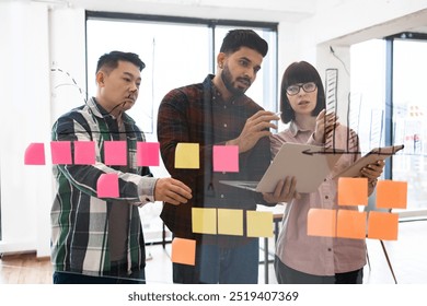 Colleagues collaborating on project brainstorming ideas using sticky notes on glass wall. Teamwork, communication, and creativity are emphasized. Modern office setting. - Powered by Shutterstock