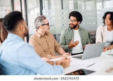 Colleagues converse around a laptop, with one member explaining a concept, the team's attention and open body language indicate a collaborative and receptive work setting - Powered by Shutterstock