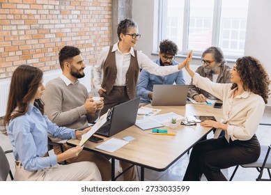 Colleagues from different generations and backgrounds achieving shared goals, showing synergy and winning spirit in a modern workspace