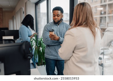 Colleagues enjoying a coffee break, engaging in casual conversation by the office window - Powered by Shutterstock