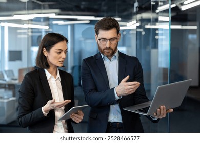 Colleagues in formal attire engage in business discussion using laptop and tablet. Creative workspace setting highlights team communication and project management in modern office. - Powered by Shutterstock