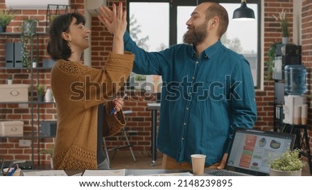 Colleagues giving highfive while brainstorming ideas to design project and plan marketing strategy. Man and woman celebrating success at research meeting, showing unity in startup office.