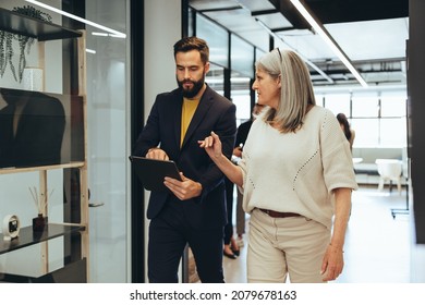 Colleagues having an important discussion while walking together in an office. Two diverse businesspeople using a digital tablet in a modern workspace. Entrepreneurs collaborating on a project. - Powered by Shutterstock