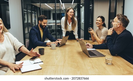 Colleagues laughing cheerfully during a meeting in a boardroom. Group of happy businesspeople enjoying working together in a modern workplace. Successful business professionals collaborating.