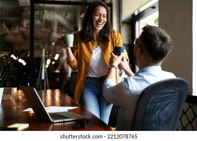Colleagues laughing in office. Businesswoman and businessman drinking coffee