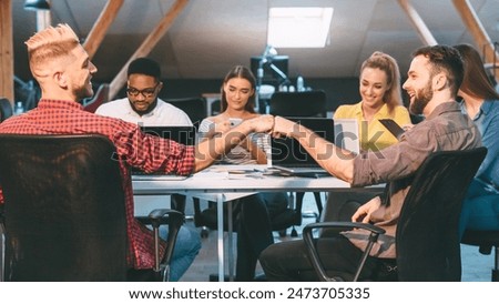 Colleagues in a loft office engage in teamwork, with two men sharing a fist bump, highlighting a positive and collaborative work environment.