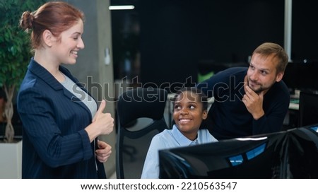 Colleagues look at the monitor and decide working moments. African young woman, caucasian man and red-haired caucasian woman communicate in the office. 