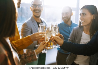 Colleagues in the office celebrate the concluded deal with champagne and sparkling wine. A group of people with glasses of champagne having fun, relaxing in the office. Concept of work, holiday.