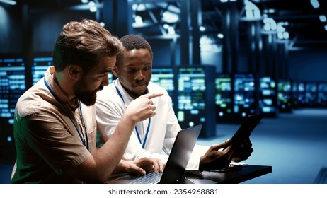 Colleagues running data center electronics diagnostic tests to determine and patch software issues. Mechanics using laptop and tablet to repair critical systems, checking for flaws - Powered by Shutterstock