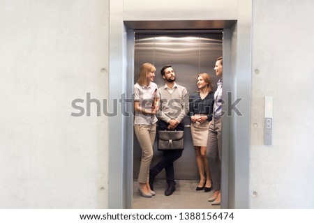 Colleagues talking while standing in elevator at office