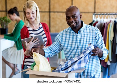 Colleagues using digital tablet while sorting clothes from donation box in the office - Powered by Shutterstock