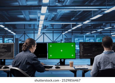 Colleagues working on green screen desktop PC in data center housing storage infrastructure. Coworkers using mockup computer display in server hub workspace filled with networking tech